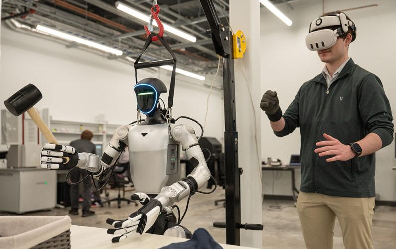 Person wearing a virtual reality headset controlling a humanoid robot equipped with tools in a laboratory setting.