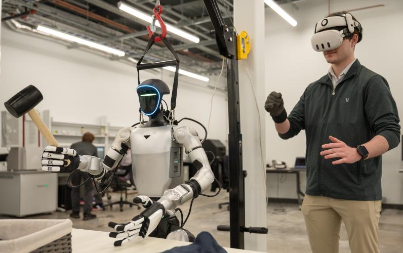 This is an image of someone using VR goggles and a glove to control a humanoid robot holding a rubber mallet.